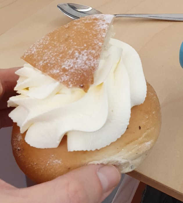 Semla med vispad grädde och mandelmassa delad med en sked, på ett fat.