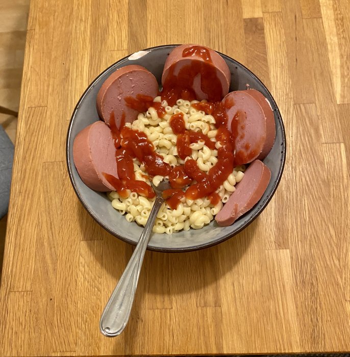 En skål med snabbmakaroner och skivad basturökt korv toppad med ketchup.