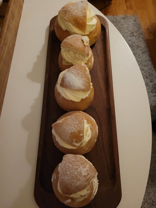 Semlor med mandelmassa och vispgrädde på en träbricka.