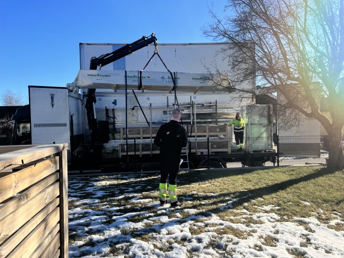 Leverans av uterumskomponenter från Willab Garden med lastbil och kran, personer dirigerar leveransen.