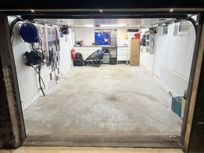 Organiserat garage med verktyg, hyllor och arbetsbänk, sett från garagedörren.