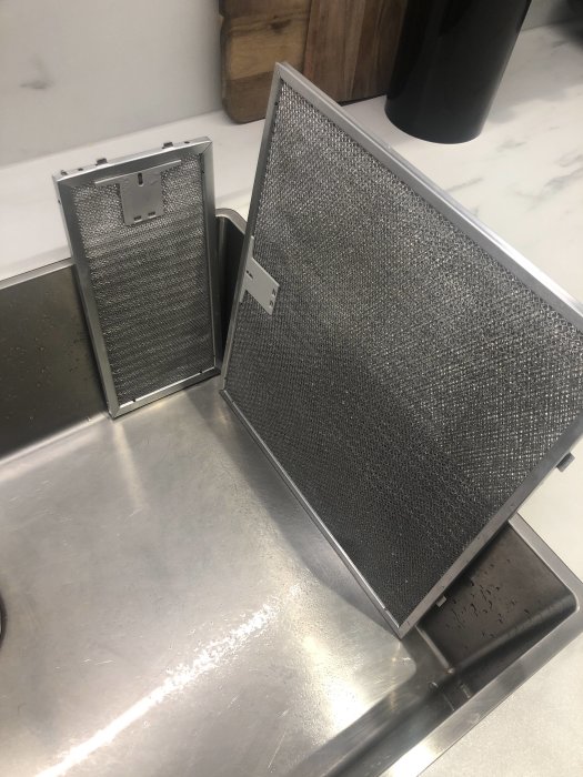 Två metallfläktfilter står på ett köksbänk av rostfritt stål.