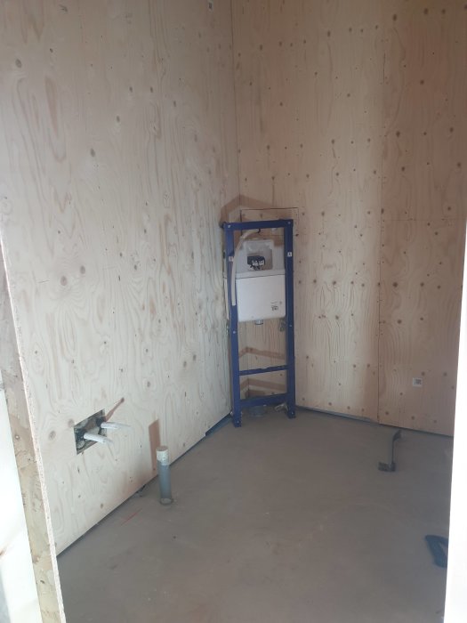 Renoveringsarbete i rum med OSB-skivor på väggar, synliga rör och elinstallationer samt markerat dörrhål.
