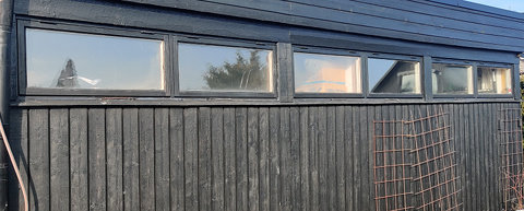 Takförsedda dubbelfönster på en svartmålad garagefasad under klart väder.