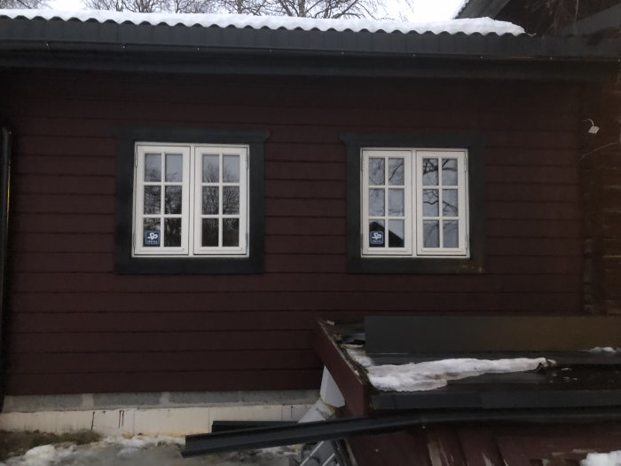 Renoverat hus med nyinstallerade fönster och foder, oavslutad fasad med snö och byggmaterial i förgrunden.