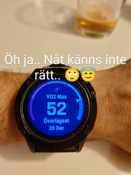 Pulsklocka visar VO2 Max-värde 52 med texten "överlägsen" och datum, bakgrund med suddigt glas.