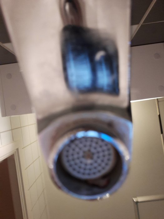 Suddig närbild av en vattenkran med synligt filter och möjliga rester av en gammal strålsamlare inuti.