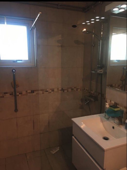 Renoverat badrum med nyinstallerad genomskinlig duschvägg i glas och handfat.