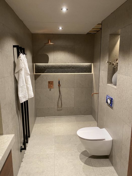 Modernt badrum under renovering med dusch, toalett och kaklade väggar.