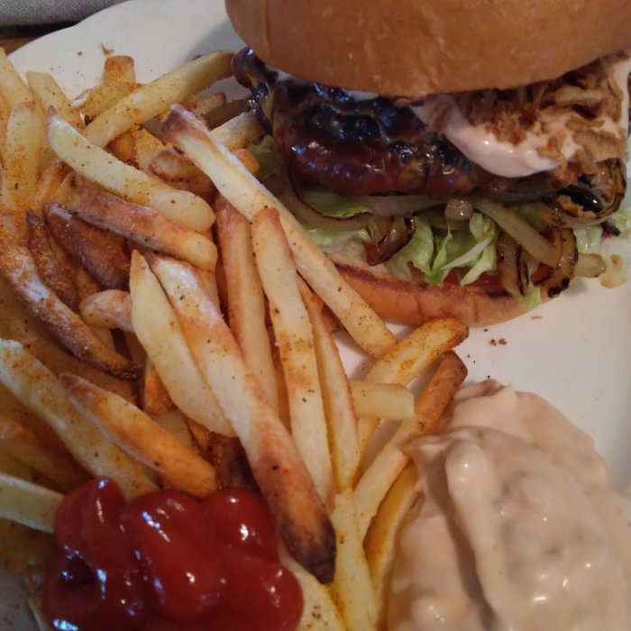 Hamburgare med sallad och sås, pommes frites med ketchup och vit sås på en tallrik.