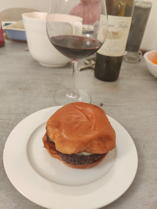 Hamburgare på tallrik med ett glas rött vin och en flaska i bakgrunden.