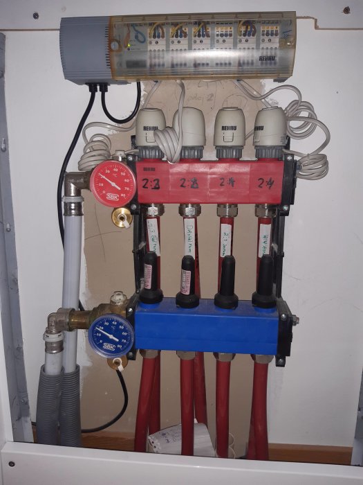 Vattenburen golvvärmefördelare med termostater och rör anslutna, märkt REHAU, inomhus.