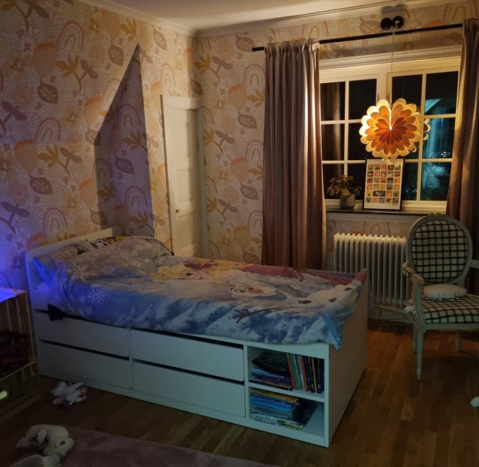Ett barnrum på kvällen med tänd lampa, färgglatt tapetserade väggar och en säng med Frost-bäddset.