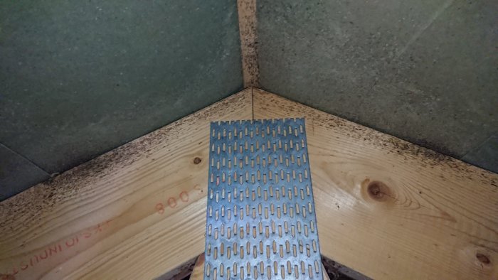 Svarta prickar synliga på en takstol med en metallplåt nedanför, tecken på fuktskador eller mögel i en husvind.