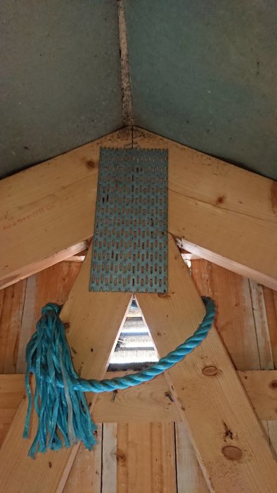 Takstolar på en vind med synliga svarta prickar nära ett ventilationsgaller och en blå repknut, tecken på möjlig fukt-skada.