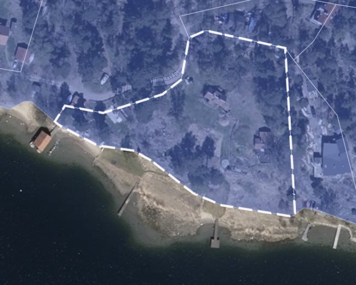 Satellitbild över kustnära fastighet markerad med vita linjer för tomtgränser, inkluderar byggnader och bryggor.