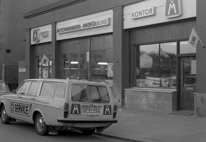 Svartvit bild av en Volvo servicebil parkerad utanför en Motormännens Riksförbundskontor med skyltar.