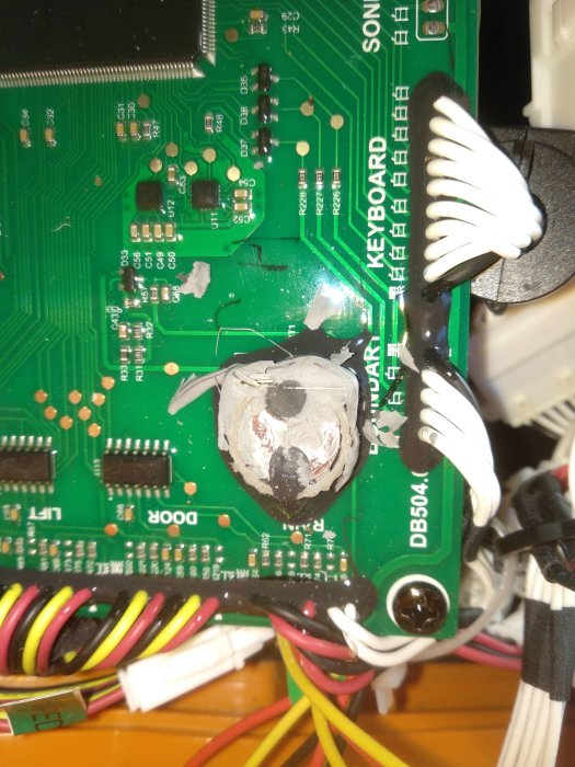 Elektronikkort med lödade komponenter och två svarta gummibitar på ovansidan nära ett batteri.