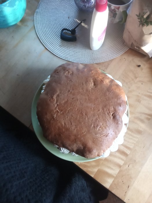 Hembakt bröd på ett fat på köksbord med mjölpåse och kryddflaska i bakgrunden.