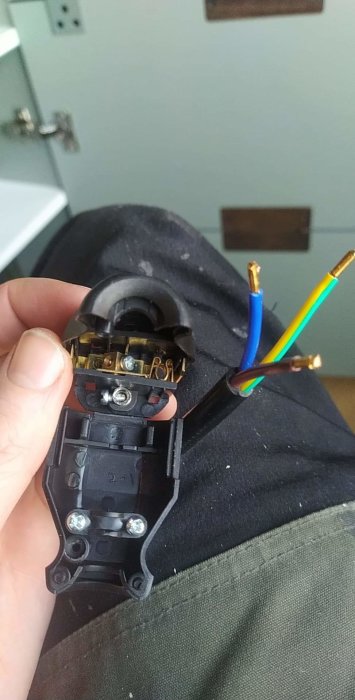 Hand håller en oansluten elkabel och en elektrisk kontakt med synliga anslutningspunkter.