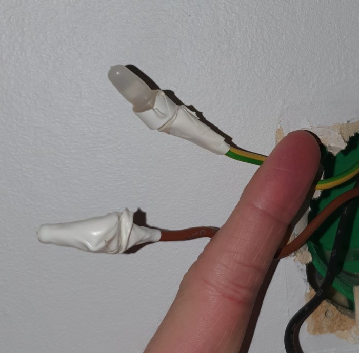 Finger pekar på improviserat isolerade elektriska kablar med eltejp vid vägginstallation.