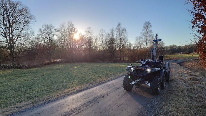 ATV med släp och underhållsutrustning på en grusväg i landskap med morgonsol.