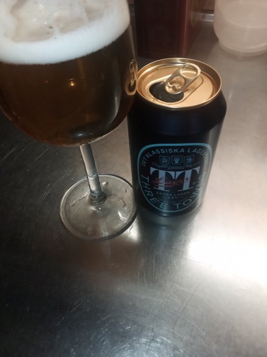 Ett glas med ljust öl bredvid en öppnad ölburk med texten "Extra Lager" på ett köksbänk.