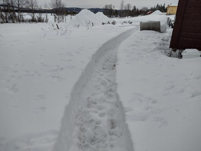 En nyskapad gång i snön mellan två byggnader på en gård i vinterlandskap.