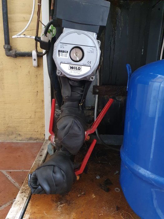 Värmesystemets cirkulationspump monterad vertikalt med anslutna rör och elektrisk kabel.