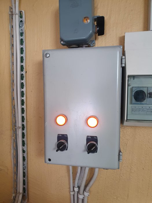 Elcentral med två lysande varningslampor och vred, indikerar att värmepumpen fungerar.
