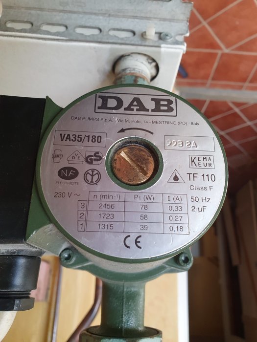 Värmepumpsmärke DAB i funktion, teknisk etikett synlig, kopparanslutning och vägg i bakgrunden.