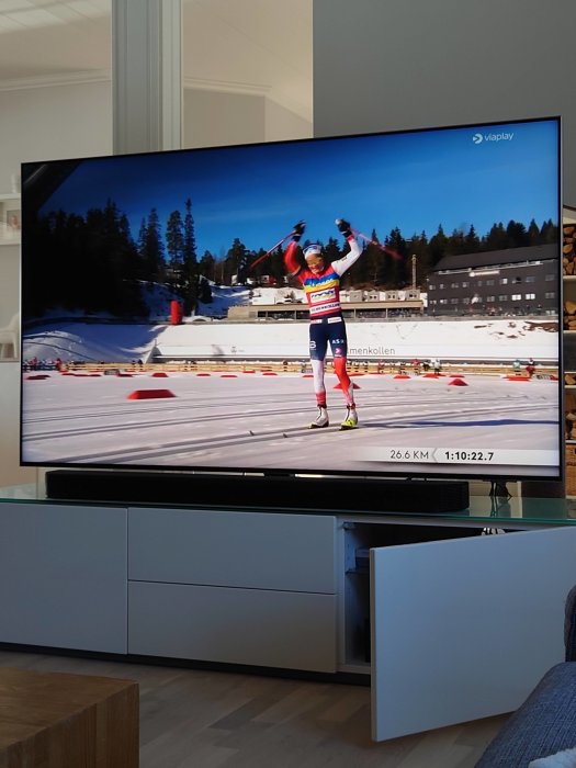 En skidåkare firar vid målgång på en TV-skärm med texten "Holmenkollen" och "viaplay" synlig.