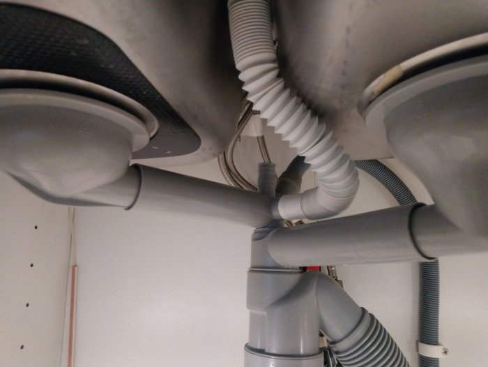 Undervy av köksskåp som visar rörkopplingar och avlopp från en köksdisk med synlig läckagepunkt.