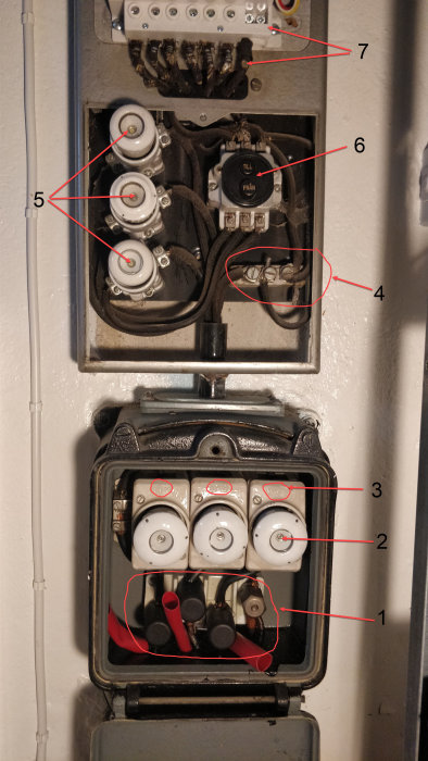 Öppet elskåp med gammal elmätare, säkringar och synliga metalltrådar markerade med nummer för diskussion.