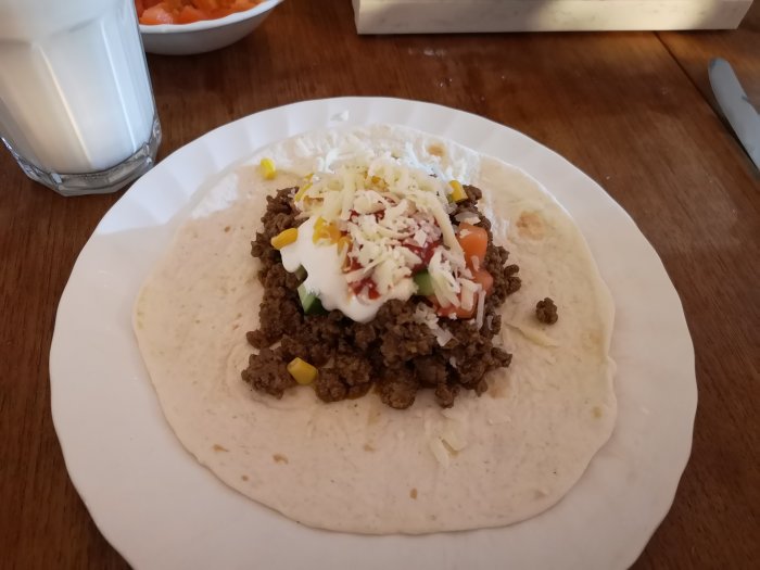 Öppen taco med köttfärs, ost, majs, sallad och sås på en tallrik, redo att ätas.