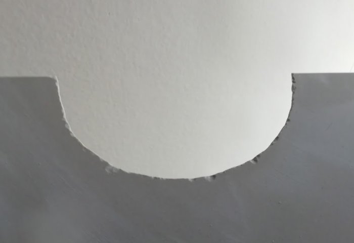 Ojämn utsågad cirkelform i vit vägg med oregelbundna kanter och sprickor.