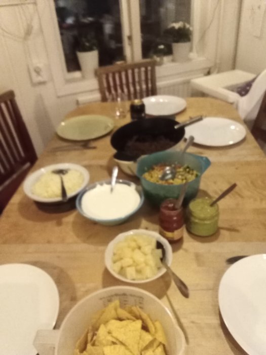 Ett dukat bord med ingredienser för tacos, inklusive tortillachips, salsa och guacamole.