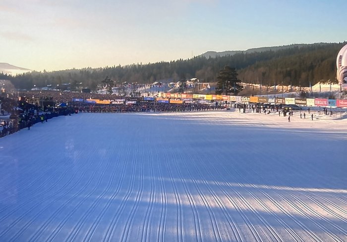 Välpreparerad slalombacke med skidåkare och publik vid foten i vinterlandskap.