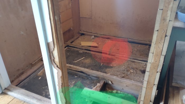 Renoveringsarbetsplats med markerade områden för toalett i rött och handfat i grönt, synligt bjälklag och svart papp.
