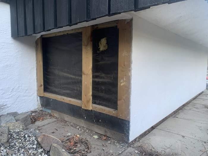 Delen av ett hus ovan jord med exponerad isolering och träreglar som förberedelse för tilläggsisolering.