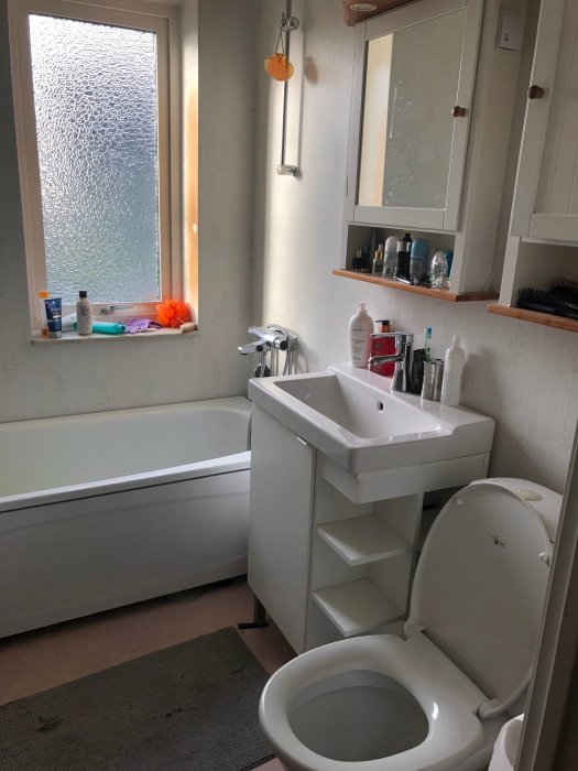 Renoverat badrum med frostat fönster, handfat, toalett, badkar och handdukstork.