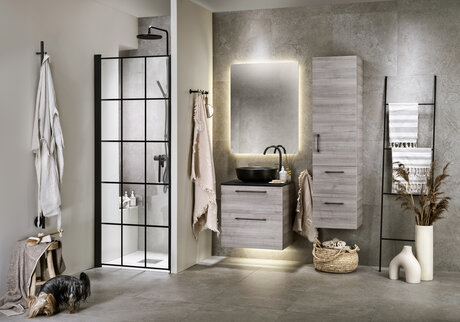 Modernt badrum med grå kakelväggar, svart spröjsad duschdörr, svart diskbänk och träskåp.