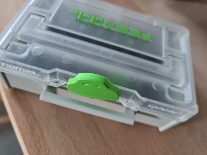 Stängd, transparent bits-box med grönt lås och Festool-logga, ligger på bordet.