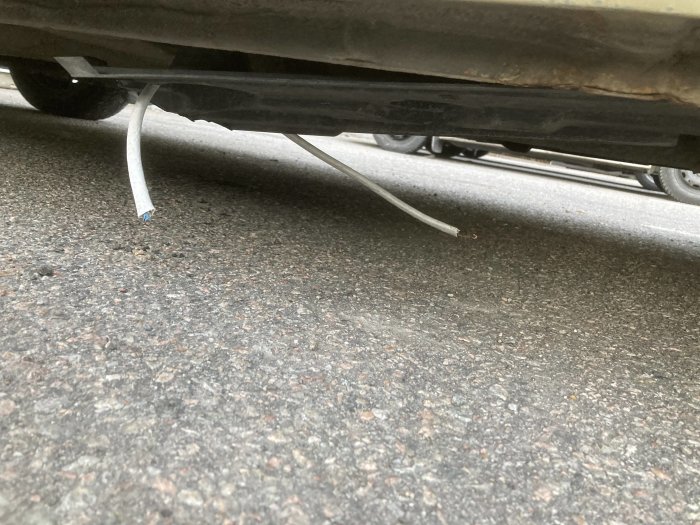 Underbilsskydd hänger löst från en bils underrede på asfaltsyta.