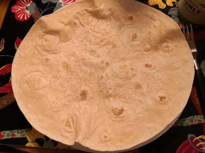 En uppvärmd vetetortilla på en färgglad bakgrundsduk med en gaffel vid sidan.
