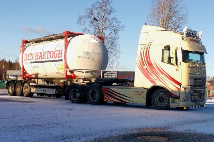 Lastbil med tankcontainer parkerad på en snötäckt väg under solig himmel.