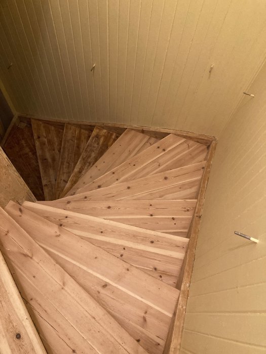 Trappa med oprimerade trästeg och vitmålade väggar, i ett hus under renovering.
