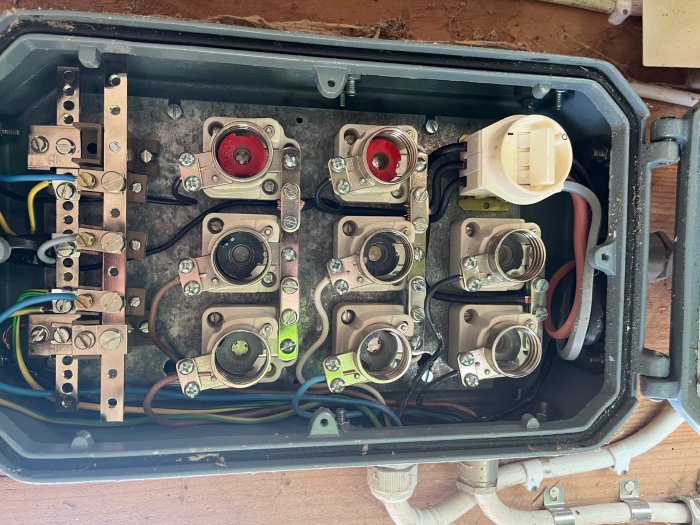 Öppen elcentral med 3x2 porslinssäkringar och anslutna kablar i en ladugård.