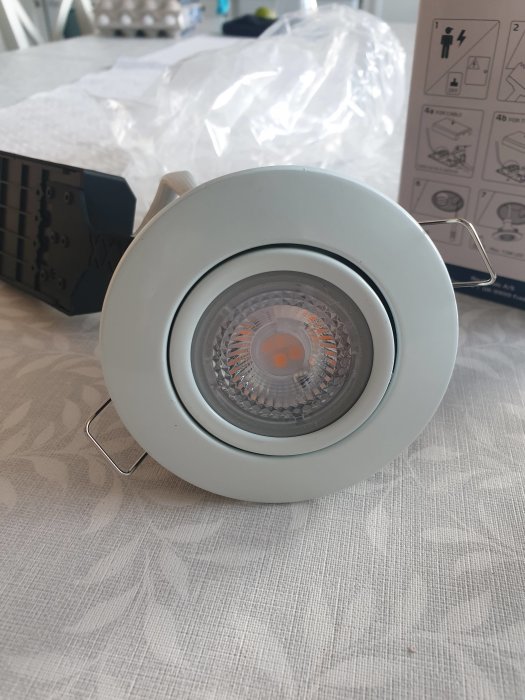 Spotlight med stor ytterdiameter på en vit duk, inplastning och manual syns i bakgrunden.