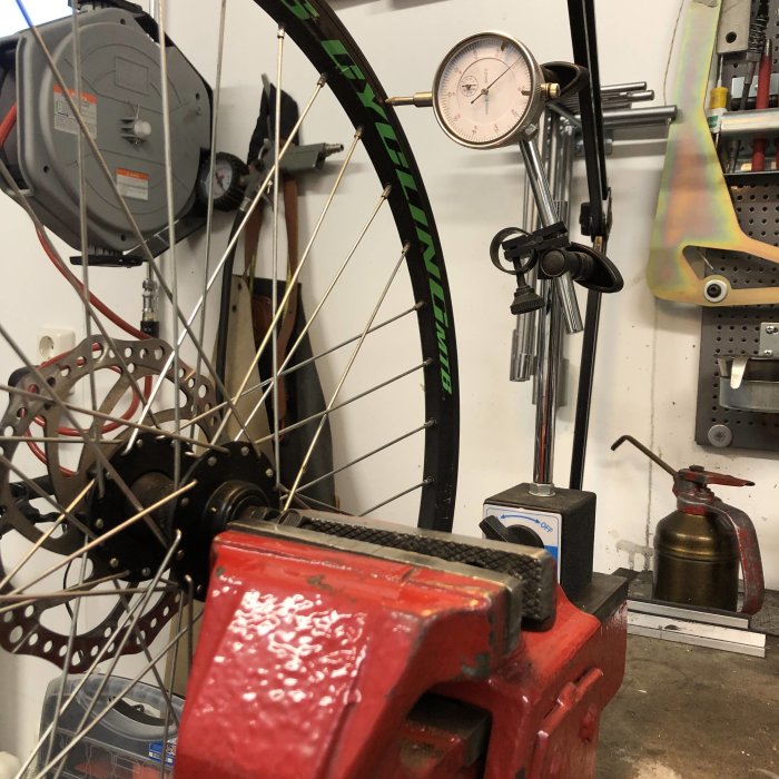 Mountainbikehjul fastspänt i skruvstycke med mätverktyg för att kontrollera fälgen.